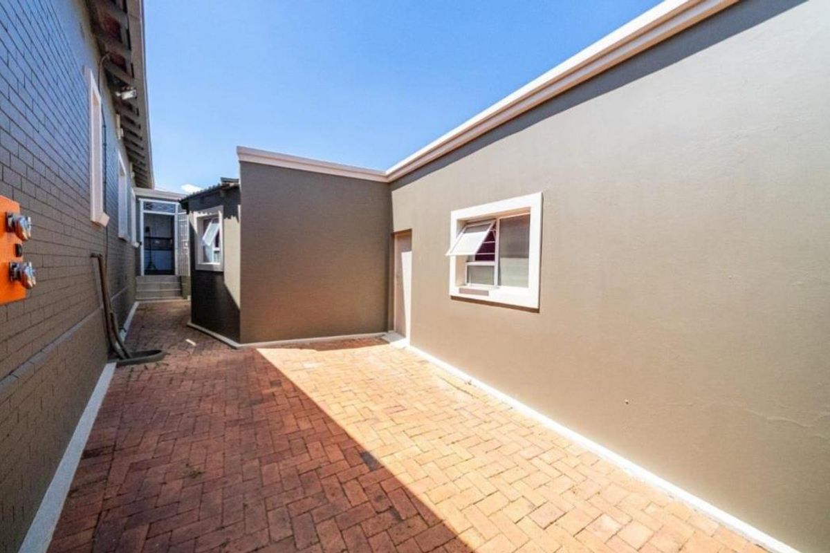 A clean, well-maintained rear courtyard area featuring brick paving and neutral-toned exterior walls with casement windows.