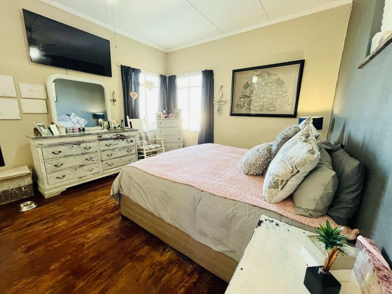 A well-lit bedroom featuring warm-toned wood flooring, neutral wall finishes, and large windows that provide ample natural light.