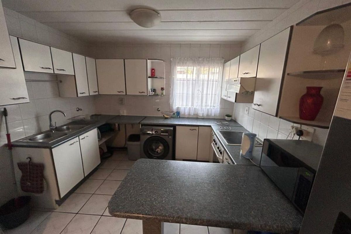 A functional kitchen featuring white cabinetry, tiled flooring, a built-in hob, and integrated laundry appliance space, offering potential for modern renovation.