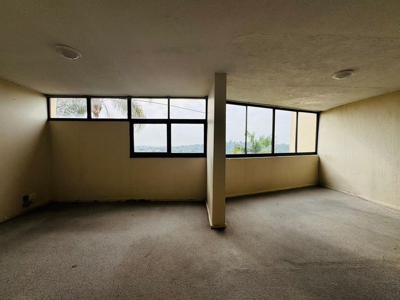 An empty, sunlit living area featuring large windows with scenic views, recessed lighting, and carpeted flooring, ready for renovation or staging.