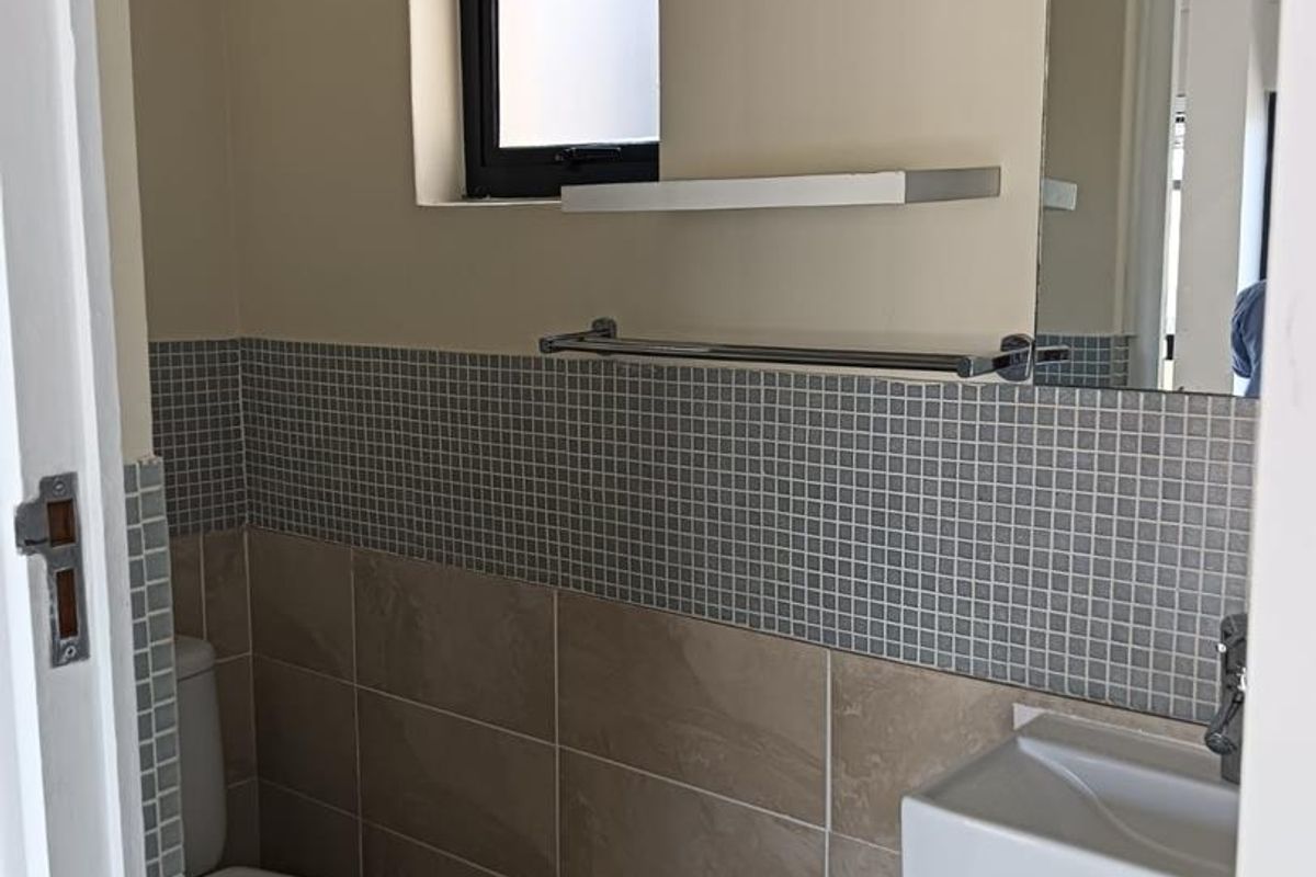 A compact, modern bathroom featuring a wall-mounted basin, toilet, tiled splashback, and a large mirror, providing a clean and functional space.