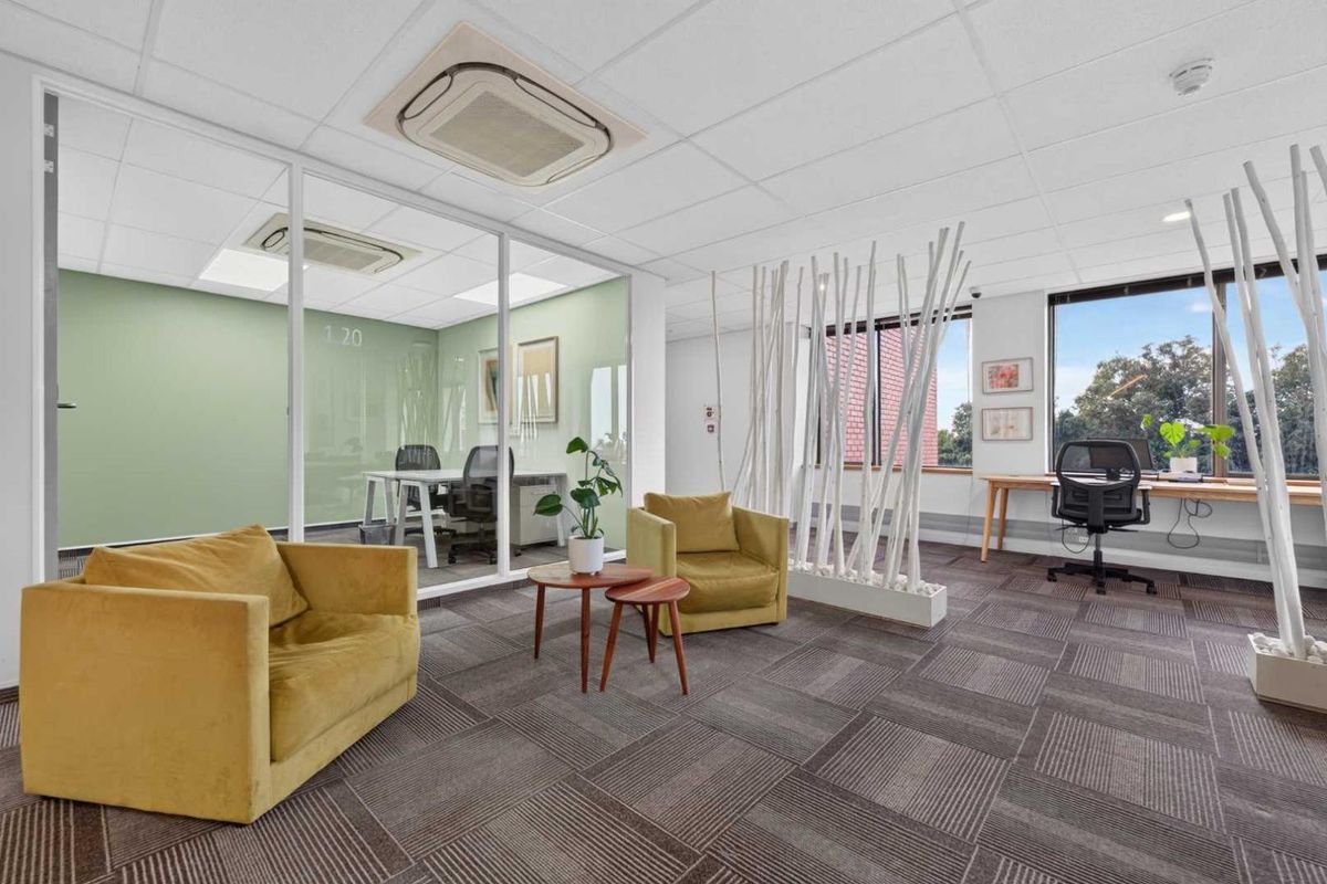 Modern office space featuring a glass-partitioned meeting room, recessed ceiling air conditioning, and large windows providing natural light and exterior views.
