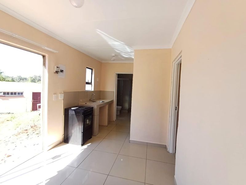 A functional, open-plan kitchen area featuring tiled flooring, a built-in sink with splashback, and direct access to the exterior.