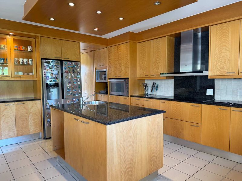 Spacious kitchen featuring extensive wooden cabinetry, granite countertops, a central island, and integrated appliances under a modern recessed ceiling.