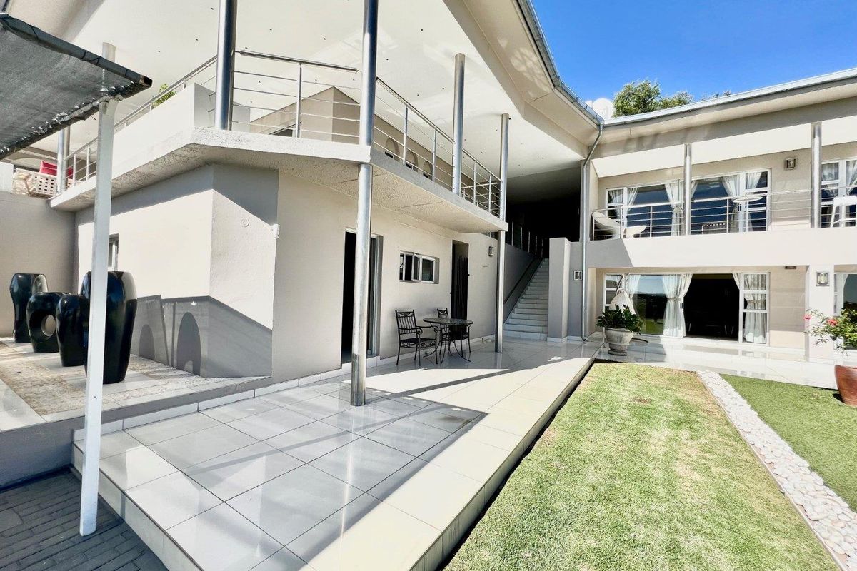 A spacious rear exterior featuring a tiled patio, stainless steel balcony railings, and an external staircase leading to the upper level.