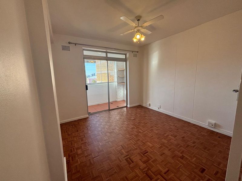 An empty bedroom featuring classic parquet flooring, a ceiling fan, and a sliding glass door providing access to a private balcony.