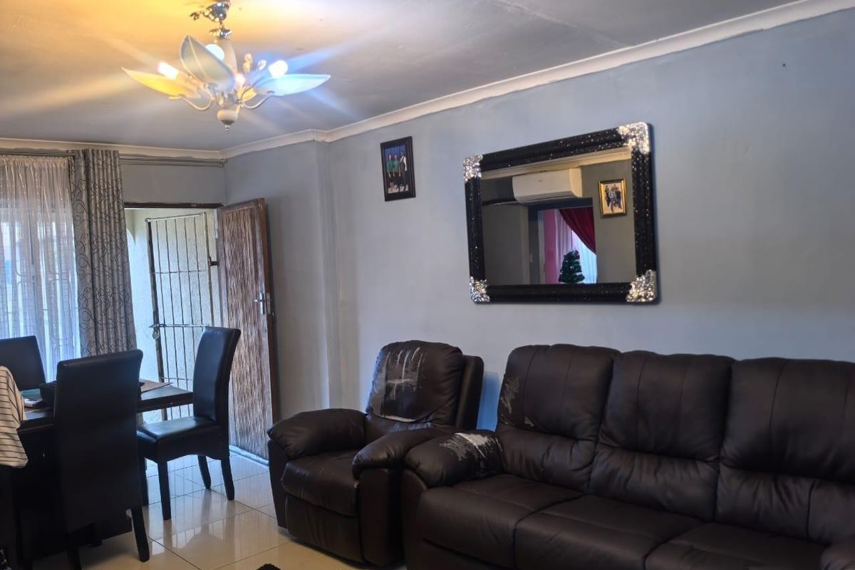 A living room featuring tiled flooring, a coved ceiling, and a wall-mounted air conditioning unit, with visible signs of wear on the ceiling and walls.