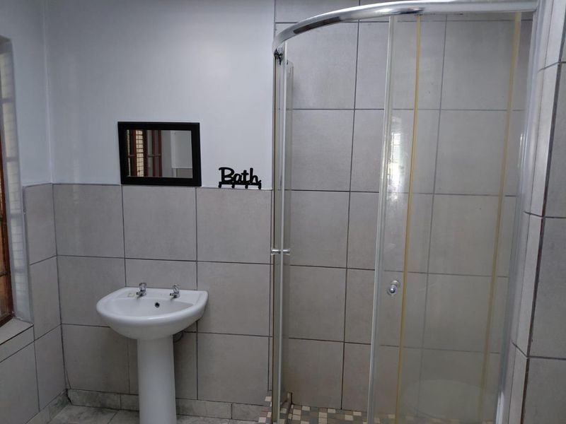 A functional bathroom featuring a pedestal basin and a glass-enclosed shower with neutral wall tiling.