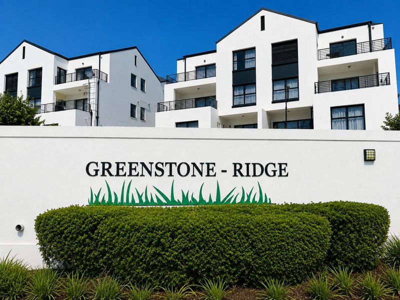 Front entrance view of Greenstone Ridge apartment complex featuring modern white facade, black metal balcony railings, and well-maintained landscaped garden.