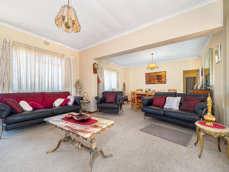 Spacious open-plan living and dining area featuring textured walls, carpeted flooring, and classic ceiling light fixtures, offering a versatile layout for family living.