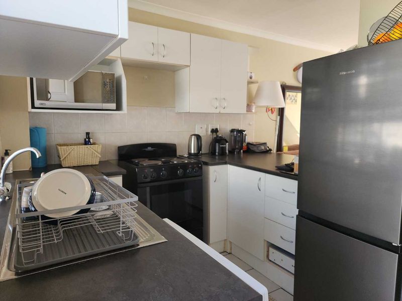 Functional kitchen featuring white cabinetry, dark laminate countertops, tiled backsplash, and a freestanding stove, offering a practical layout for daily meal preparation.