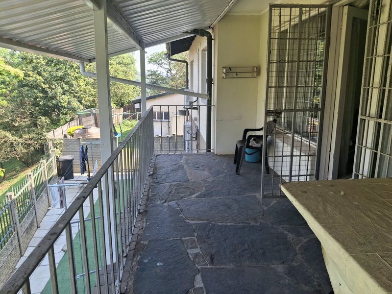 A covered balcony featuring stone flooring, metal railings, and a security gate, overlooking the rear garden area.