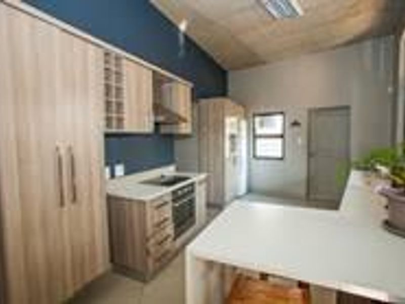 Modern kitchen featuring light wood cabinetry, stone countertops, integrated appliances, and a breakfast bar, set against a dark blue accent wall.