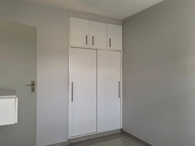 A clean, empty bedroom featuring white built-in cupboards with overhead storage and neutral tiled flooring.