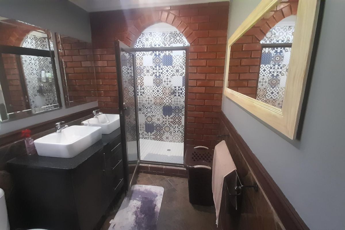 A bathroom featuring a double vanity with vessel sinks, a walk-in shower with decorative patterned tiles, and exposed brick wall accents.