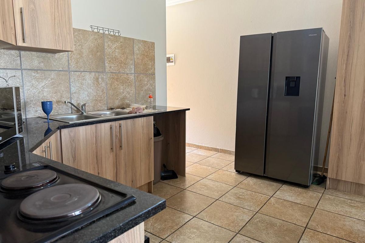 A functional kitchen featuring wood-look cabinetry, dark granite countertops, tiled splashbacks, and tiled flooring, providing a practical workspace.