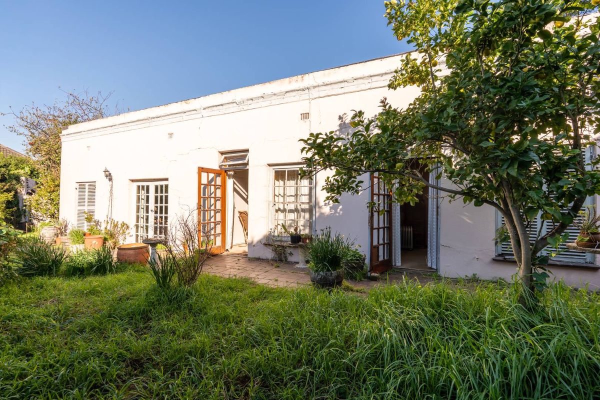 Rear view of the property featuring a paved patio area, multiple access points with timber-framed doors, and an overgrown garden space.