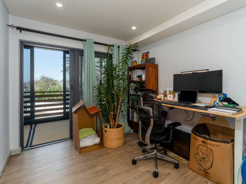 A bright home office featuring modern laminate flooring, recessed lighting, and a large sliding glass door providing access to an outdoor balcony.