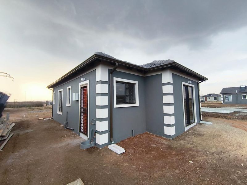 Rear view of a modern single-story house featuring a grey plastered facade with white corner detailing, sliding doors, and security gates.