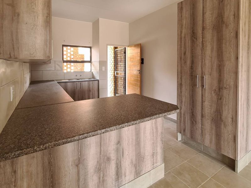 A clean, modern kitchen featuring wood-look laminate cabinetry, durable countertops, tiled flooring, and a functional layout with an integrated storage unit.