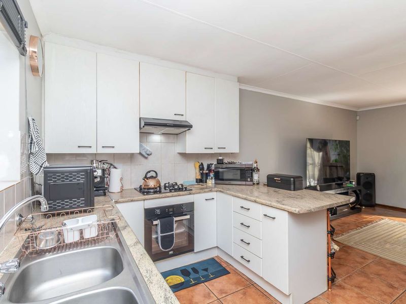 Open-plan kitchen featuring white cabinetry, granite countertops, and integrated appliances, flowing into a living area with tiled flooring throughout.