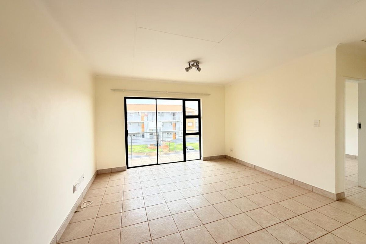 A bright, empty living room featuring neutral ceramic floor tiles and a large sliding glass door leading to a balcony.