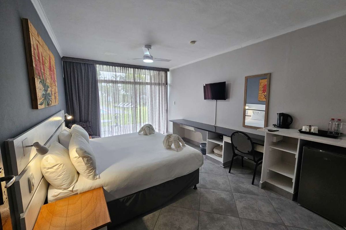 A well-maintained hotel bedroom featuring tiled flooring, a ceiling fan, built-in desk cabinetry, and large sliding glass doors leading to an outdoor area.