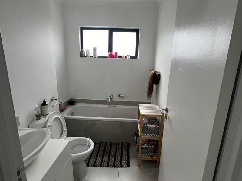 A functional bathroom featuring a built-in bathtub with tiled surround, a vanity cabinet with basin, and a toilet, finished with neutral floor tiles.