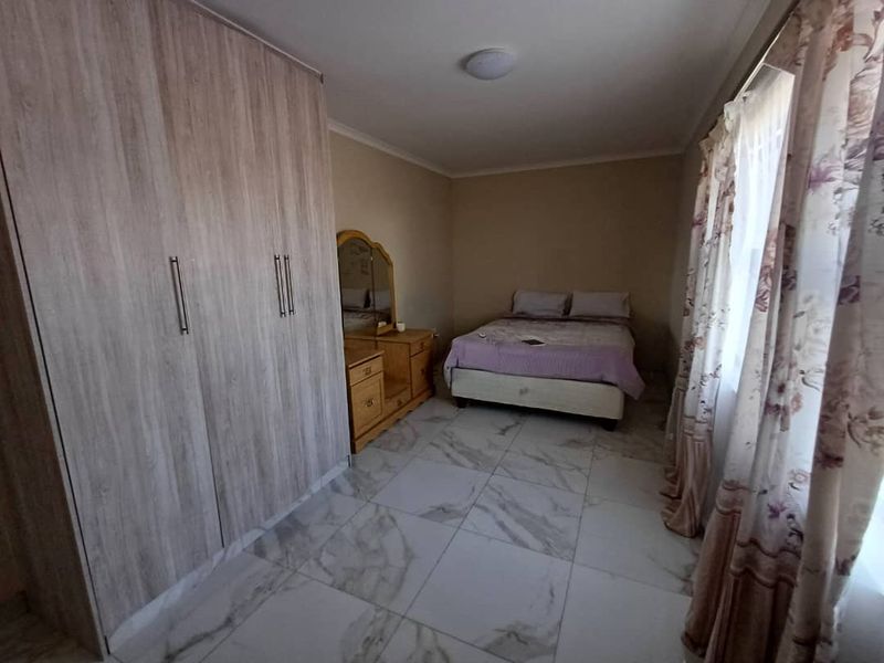 A bedroom featuring built-in wooden wardrobes and light-colored marble-effect floor tiles, providing a clean and functional living space.