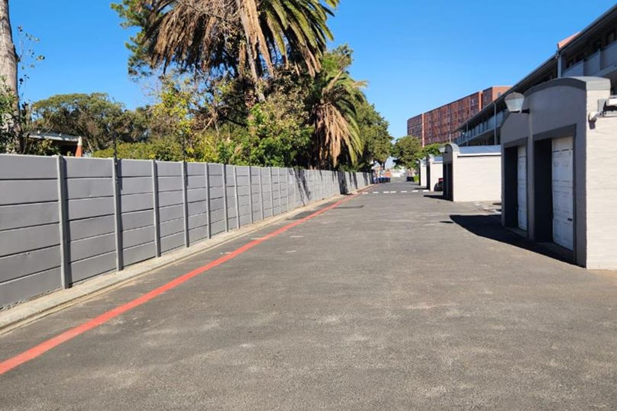 A paved driveway area featuring a perimeter boundary wall and access to garage units within the apartment complex.
