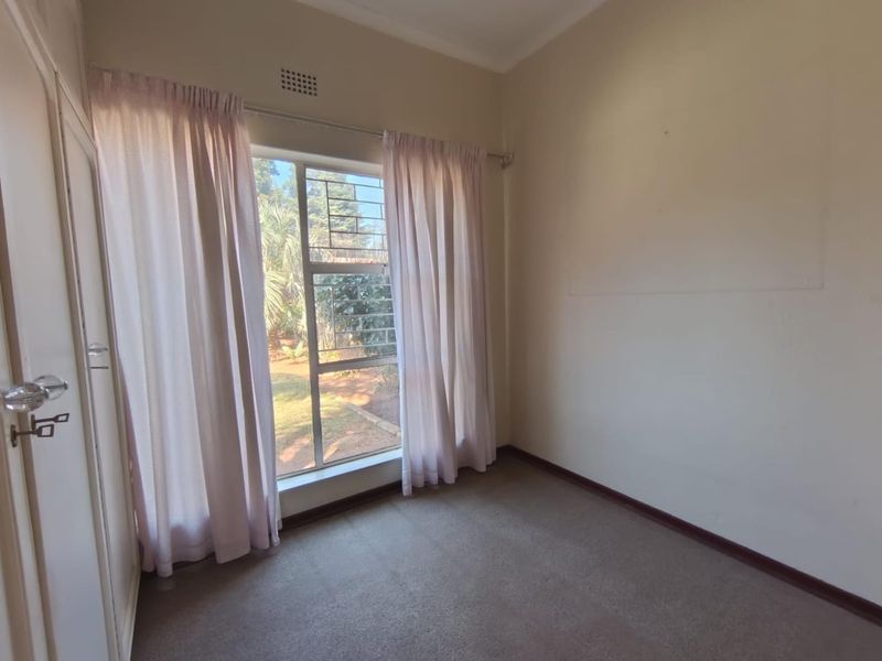 A vacant bedroom featuring carpet flooring, a built-in wardrobe, and a window with security bars overlooking the garden.