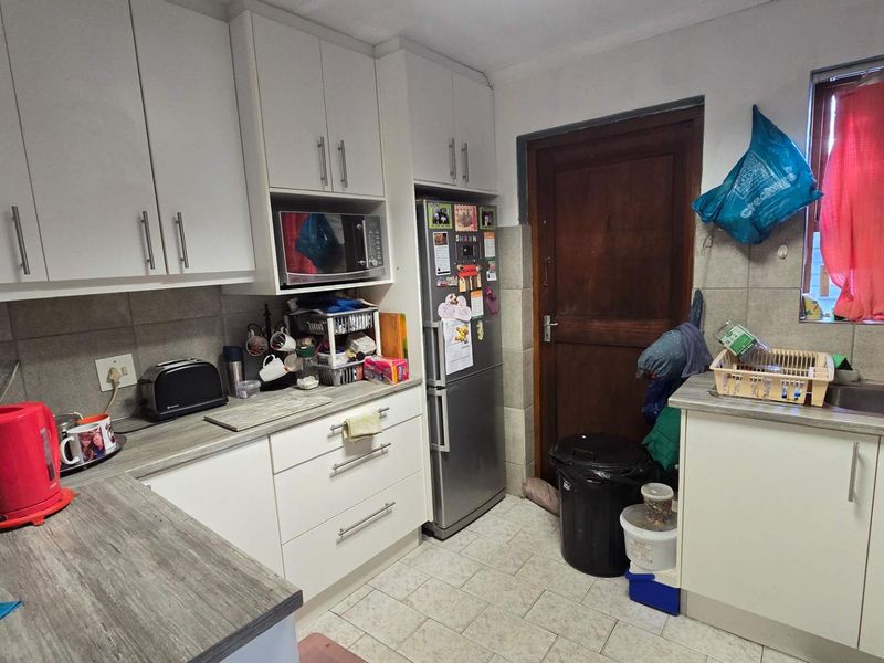 A functional kitchen featuring white cabinetry, laminate countertops, tiled backsplash, and a stainless steel sink, providing a practical workspace for daily meal preparation.
