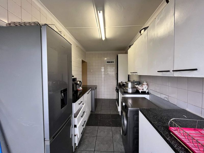 A functional galley-style kitchen featuring tiled splashbacks, granite countertops, and ample built-in cabinetry with tiled flooring throughout.