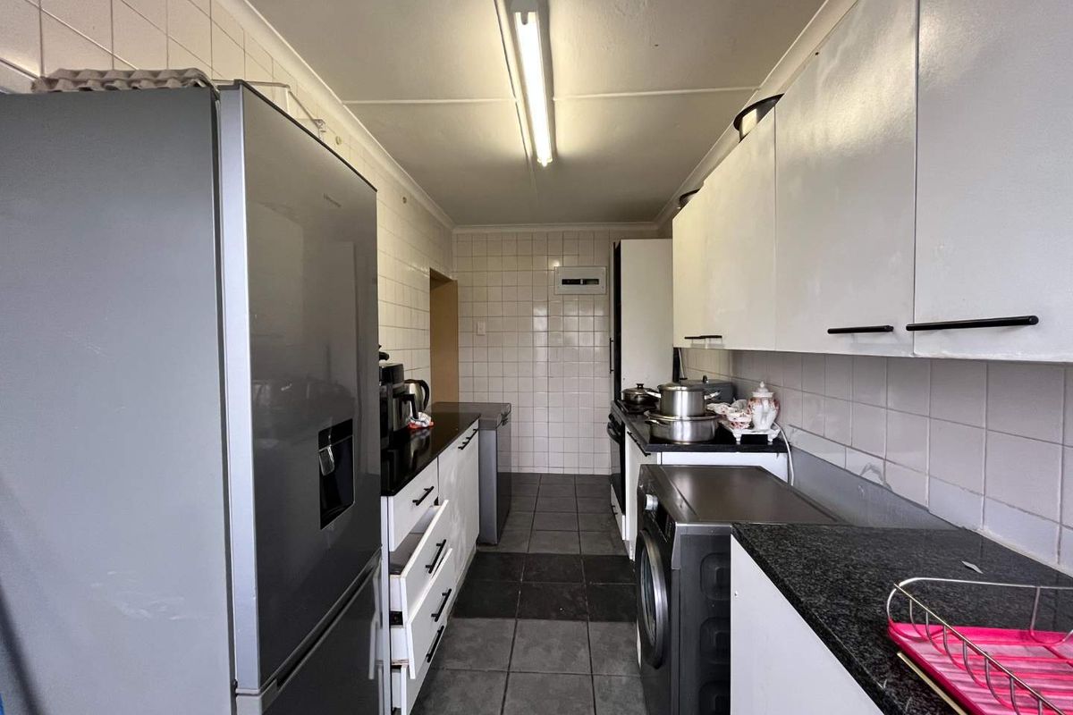 A functional galley-style kitchen featuring tiled splashbacks, granite countertops, and ample built-in cabinetry with tiled flooring throughout.