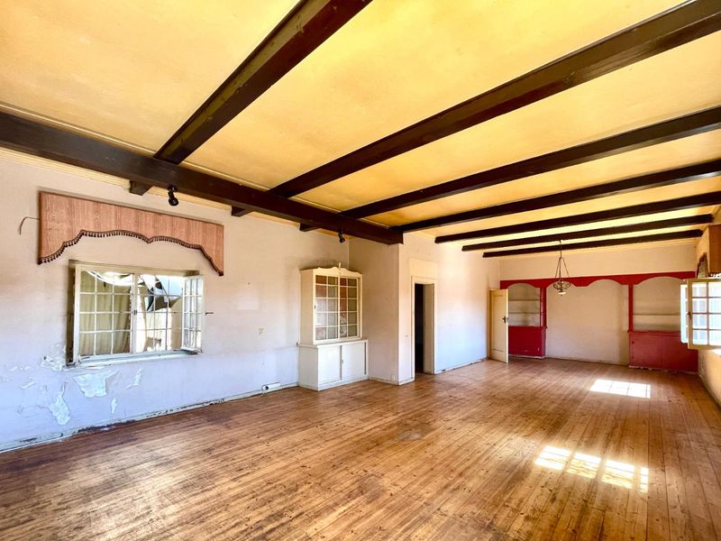 Spacious living area featuring exposed timber ceiling beams, hardwood flooring, and built-in cabinetry, requiring cosmetic renovation and repairs to wall finishes and windows.