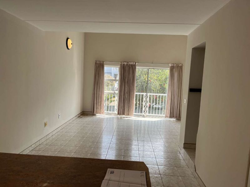 An empty, open-plan living area featuring tiled flooring and a sliding glass door that opens onto a balcony with exterior views.