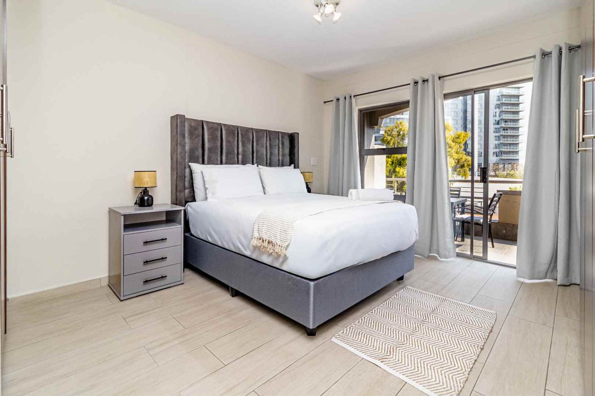 A well-maintained bedroom featuring tiled flooring, built-in cupboards, and a sliding glass door providing access to a private balcony.