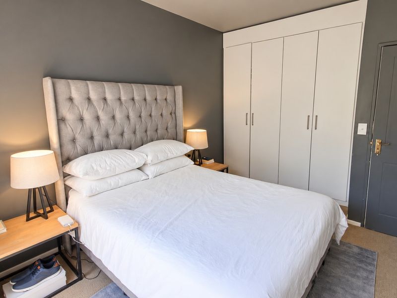 A well-maintained bedroom featuring neutral grey walls, carpeted flooring, and ample storage provided by a large built-in wardrobe.