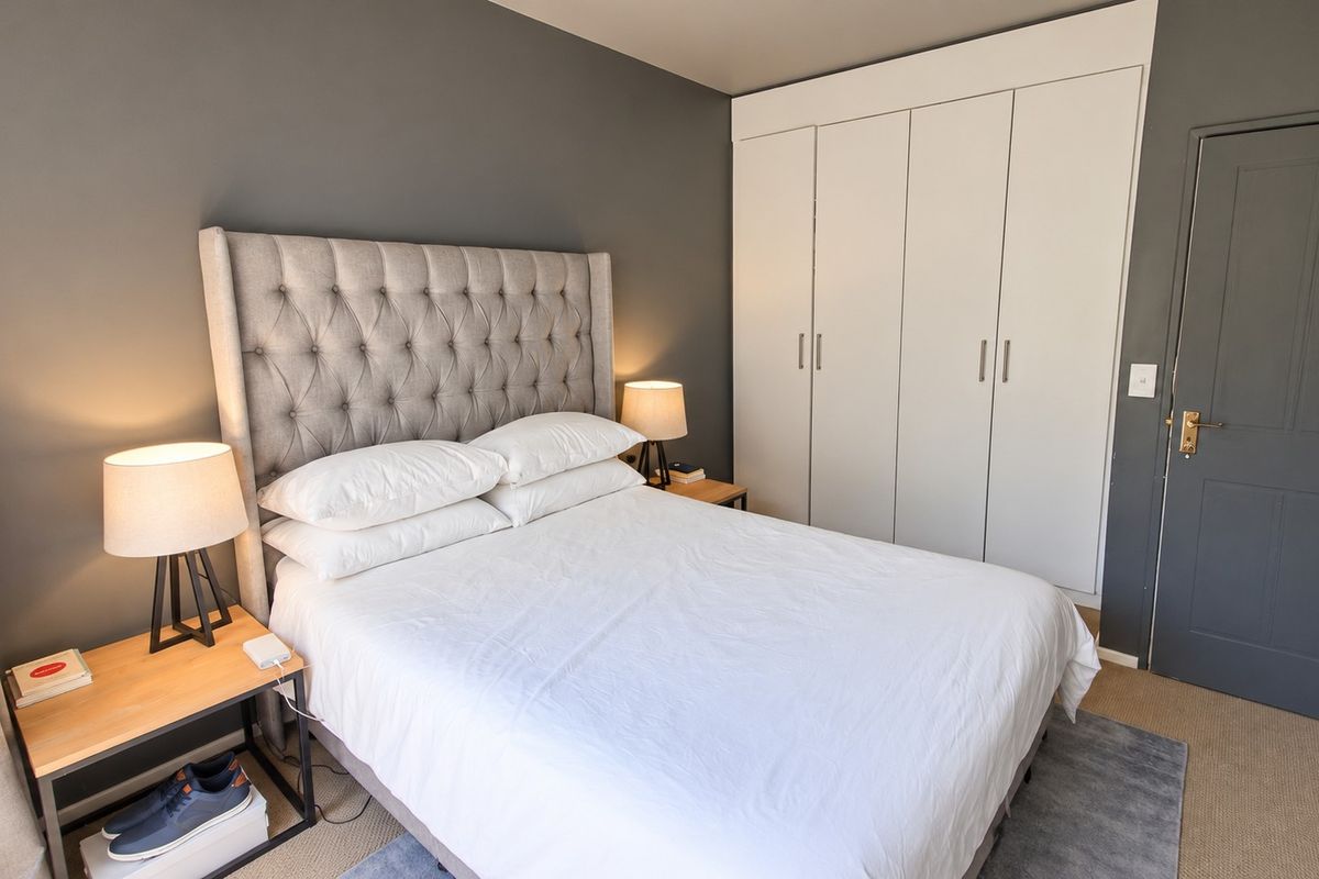 A well-maintained bedroom featuring neutral grey walls, carpeted flooring, and ample storage provided by a large built-in wardrobe.