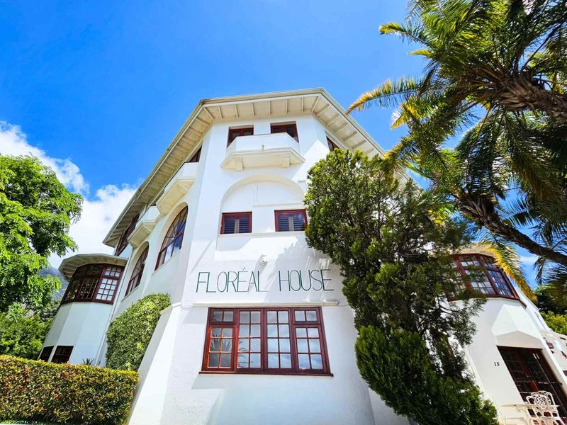 A low-angle view of the front facade of Floreal House, showcasing its distinctive architectural style, white stucco finish, and multi-pane windows.