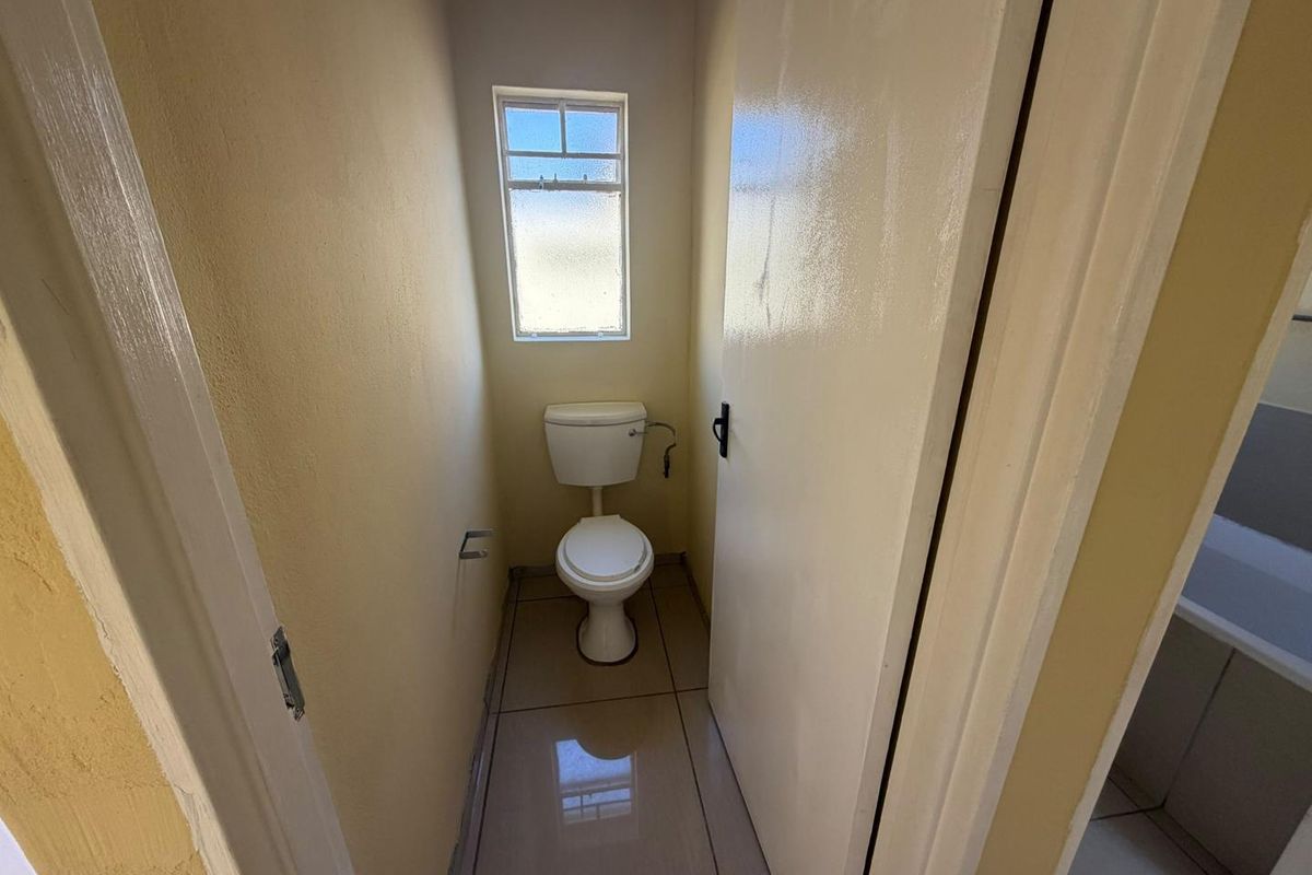 A compact, functional guest toilet featuring tiled flooring and a window for natural light.