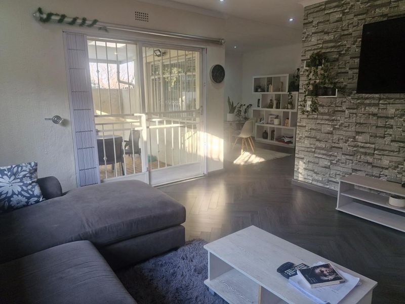 A bright living room featuring modern herringbone flooring, a textured stone veneer feature wall, and sliding glass doors leading to an outdoor patio area.