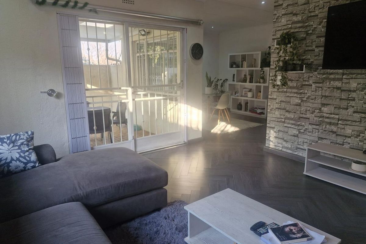 A bright living room featuring modern herringbone flooring, a textured stone veneer feature wall, and sliding glass doors leading to an outdoor patio area.