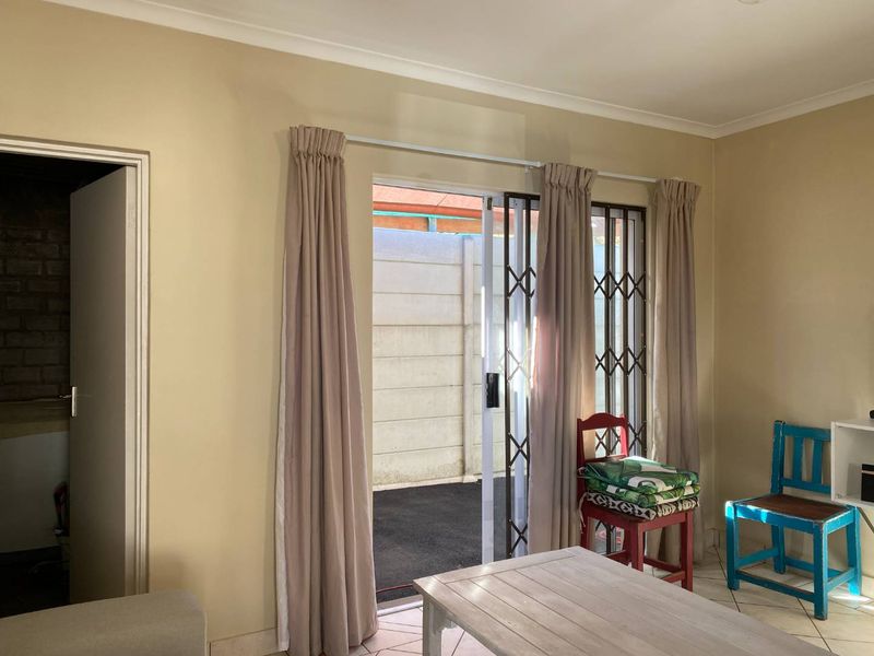 Living room area featuring tiled flooring, neutral wall tones, and a sliding glass door with security gate providing access to the exterior.