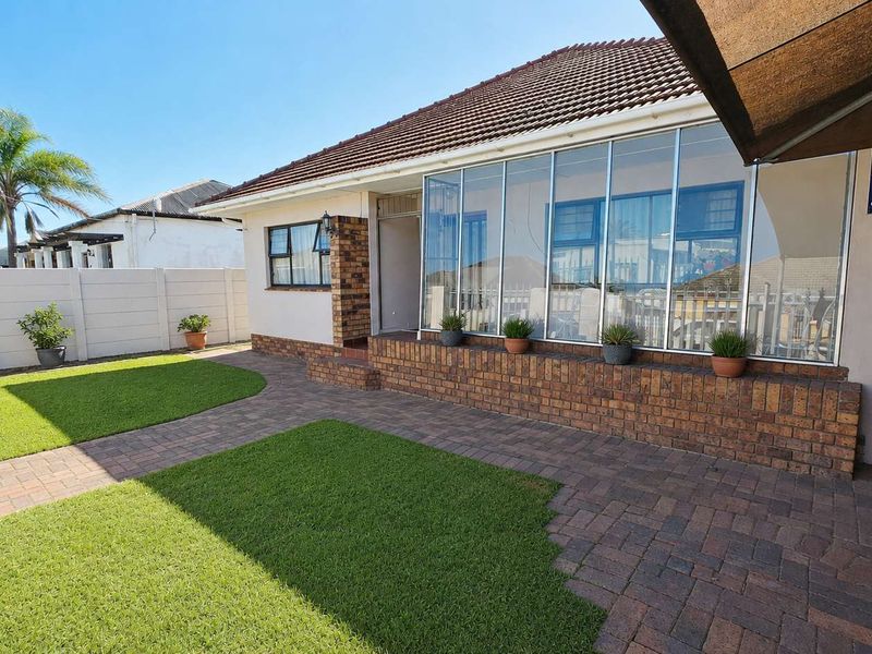 Rear exterior view featuring a paved garden area, manicured lawn, and an enclosed sunroom with large glass windows.