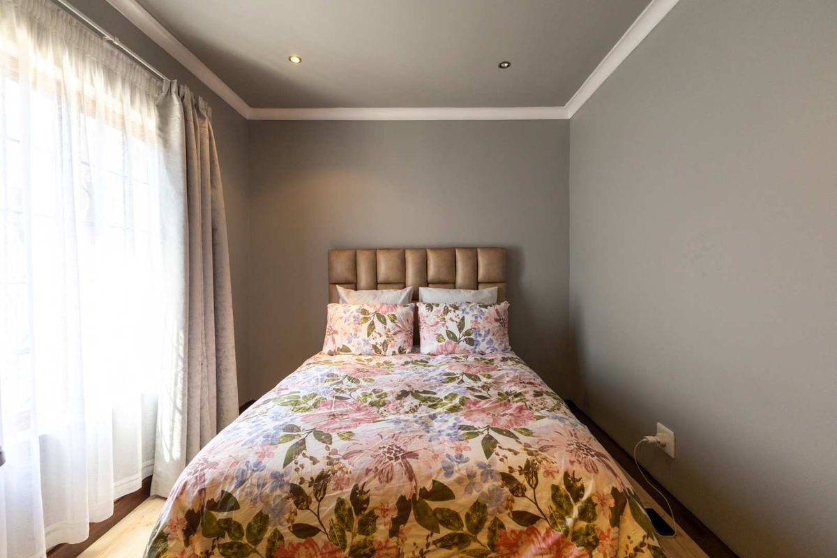 A well-maintained bedroom featuring recessed downlighting, neutral grey walls, and decorative cornice detailing.
