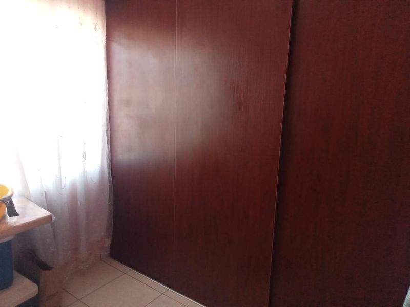 A bedroom interior featuring a large dark wood built-in wardrobe and tiled flooring, illuminated by natural light from the adjacent window.
