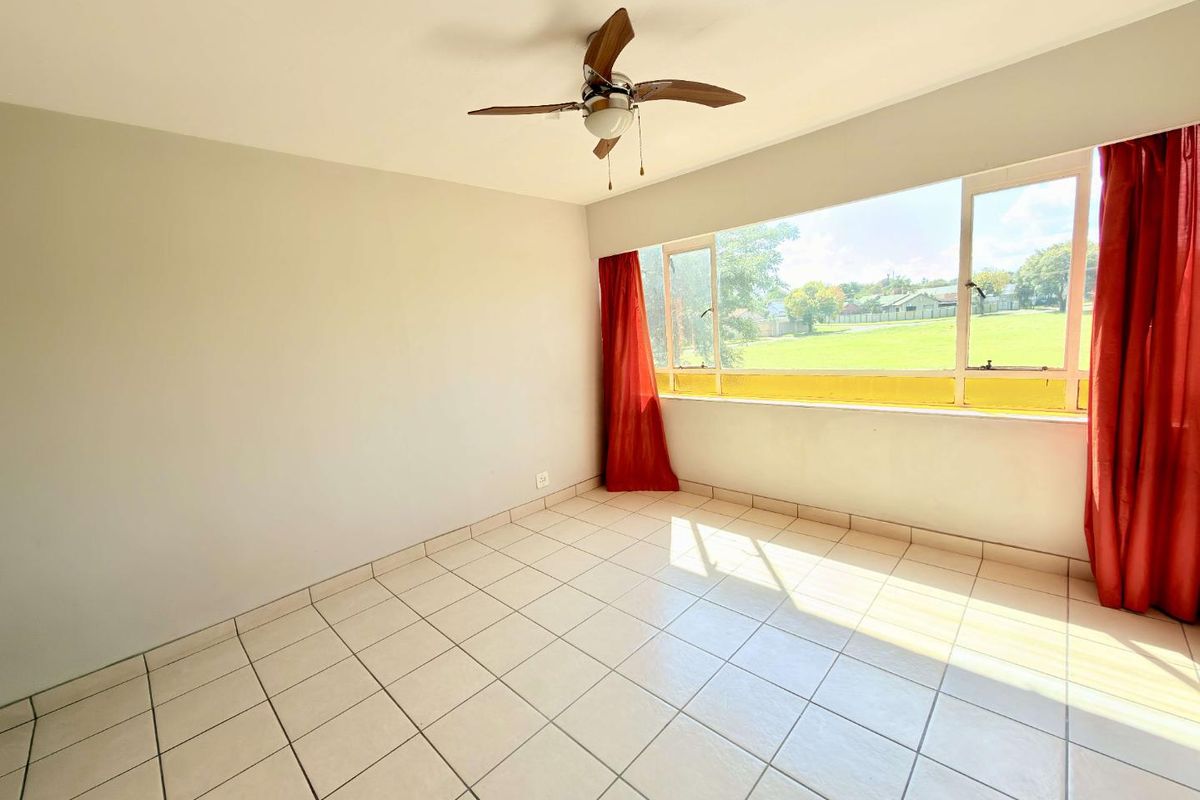 A bright, empty bedroom featuring tiled flooring, a ceiling fan, and a large window with natural light.