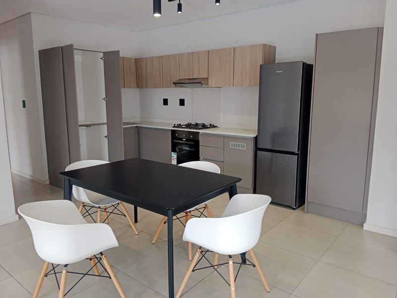 Modern open-plan kitchen featuring neutral cabinetry, stone countertops, built-in gas hob, and electric oven, seamlessly integrated with a dining area.