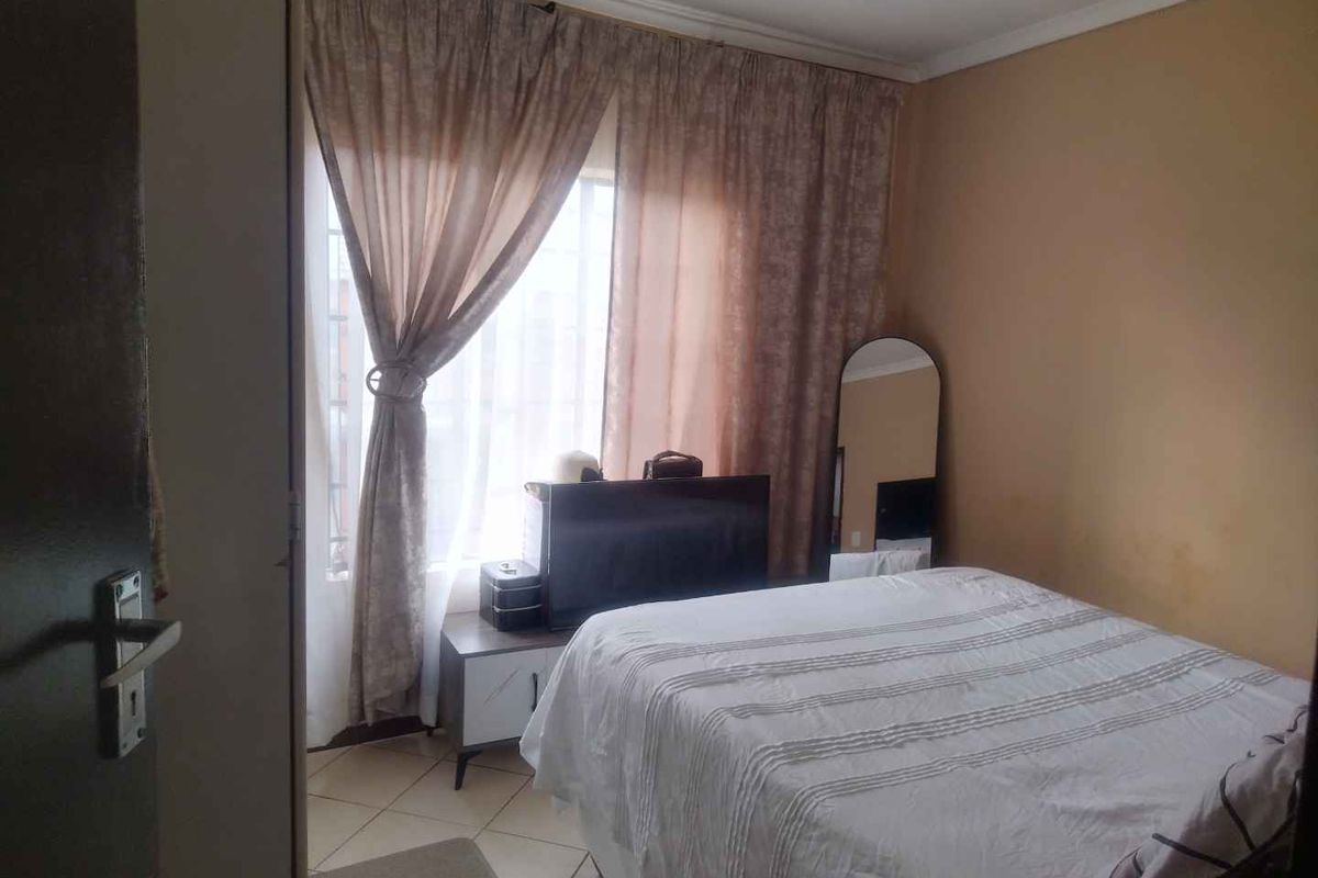 A bedroom featuring tiled flooring and window curtain rails, requiring minor cosmetic updates to the wall finishes.